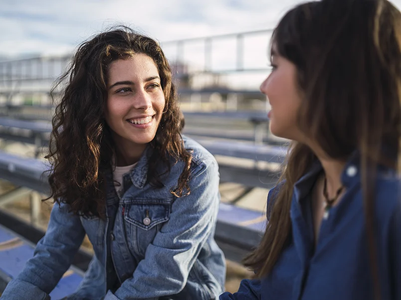 Two young women sitting on bleachers smiling and talking